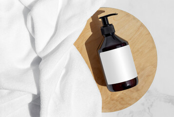 Bottle, tube, jar of shampoo, cream or lotion with white towel on the round wooden plate on a white marble. Top view. Brand commercial. Mock up. Organic eco cosmetics. Treatment spa beauty skincare 
