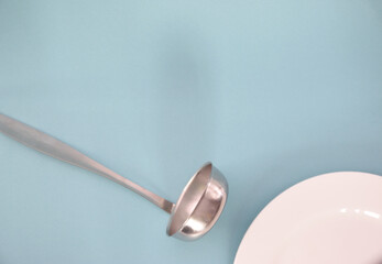 A ladle lying on the table next to a white plate