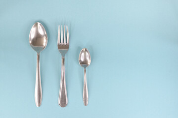 A table spoon, fork and teaspoon, laid out in a row on a light background.