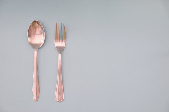 A tablespoon and fork are laid out in parallel and isolated on a light background.