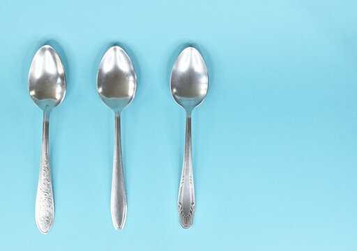 Three tablespoons lying parallel to each other and isolated on a light blue background.