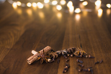 Cinnamon, star anise, cloves on dark brown wooden table and bokeh lights background, christmas concept with copy space
