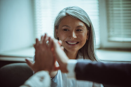 Happy Asian woman with colleagues giving five to each other during business meeting. Selective focus on smiling female face. Team building concept.