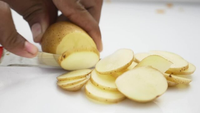 Human hands cut raw potatoes into slices