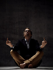 Brutal daring man in jacket, jeans, glasses and barefoot sits on floor, smoking cigarette and gesturing fucks signs