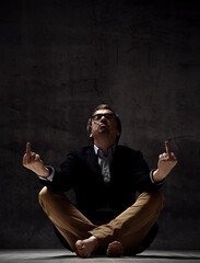 Brutal daring man in jacket, jeans, glasses and barefoot sits on floor, smoking cigarette and...