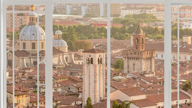Brescia cityscape as seen from a white window while birds are flying at the sunset. It is seen the capitolium, cathedral of Saint Maria assunta and the tower