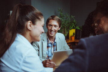 Friendly team of international people brainstorming in office. Diverse group of employees communicating during business meeting. Selective focus on smiling Caucasian business man.