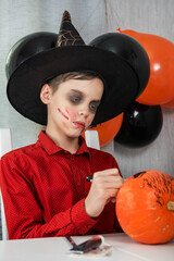 Happy teen boy in costume preparing for the Halloween celebration drawing a pumpkin. Halloween...