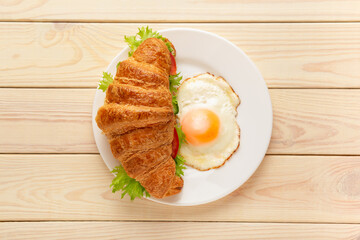 Croissant sandwich with fried egg on wooden background top view. Healthy vegetarian breakfast