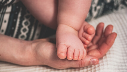 The little naked leg of the baby is carefully placed in the warm hand of the mother