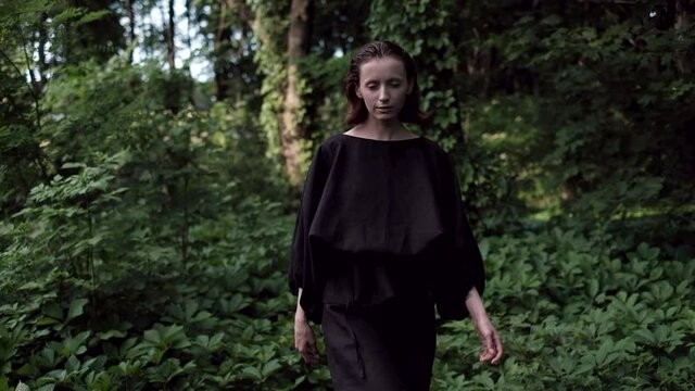 Young woman confidently walking toward the camera in the forest in the evening in slow motion