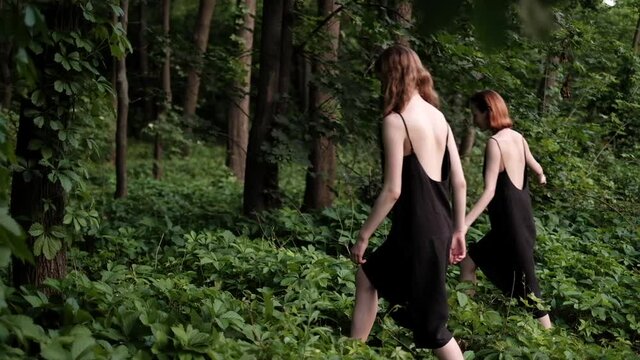 Two young women walking through the forest in beautiful black slip dresses in slow motion