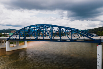 This is an aerial of a blue, eight-lane highway arch bridge that carries Interstate 64 over the Kanawha River in Charleston, West Virginia.