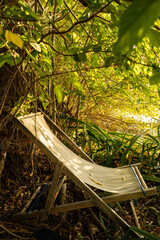 Empty deck chair in  summer sunlight under leaves next to lake