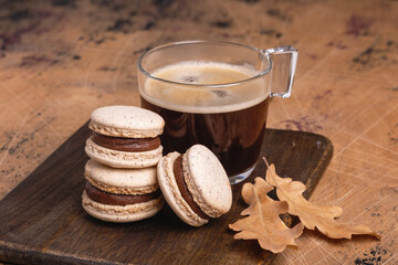 Cup of coffee and chocolate macarons on wooden background. Cozy autumn composition