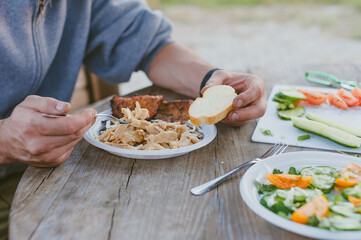 The guy eats meat at the table against the background of plates with salad.