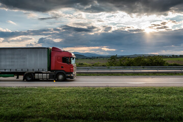 Red truck is on highway - business, commercial, cargo transportation concept, beautiful sunset sky,...