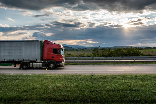 Red truck is on highway - business, commercial, cargo transportation concept, beautiful sunset sky, clear and blank space - side view