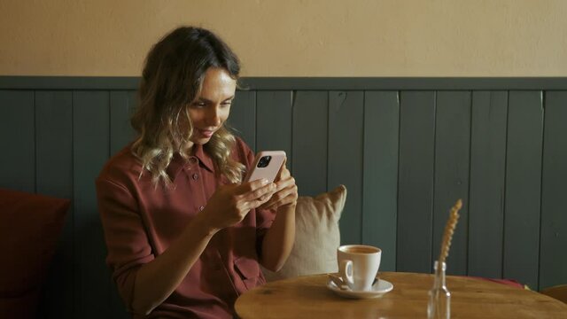 Beautiful blonde woman taking pictures of a cup of coffee with her smartphone and texting afterwards. Young food blogger with cell phone in a coffee shop. Communication, social network concept.