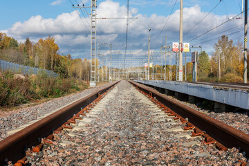 the rusty rails of the railway go into the distance in an autumn day, to the right is an empty platform. The photo is horizontal, without people.