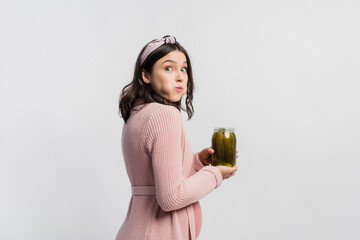 surprised and pregnant woman holding jar while eating pickled cucumbers isolated on white