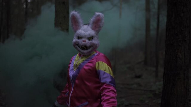 Man with horror psycho bunny mask stands with smoke grenade in the forest