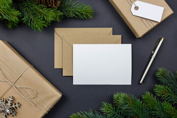Christmas table, festive styled composition. Christmas greeting cards, envelopes mock-ups. Handmade gift box, pine cones and fir tree branch on dark background. Top view. Zero waste gift wrapping.