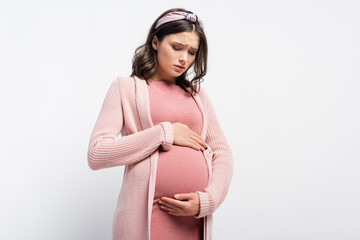 worried pregnant woman in headband touching and looking at belly on white