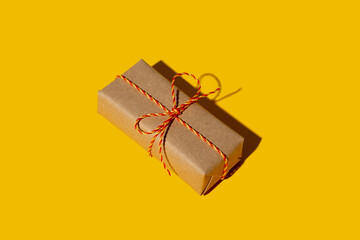 Birthday gift. Long-distance care package. Eco wrap. Holiday surprise. Vintage parcel. Rustic beige simple paper box with orange twine bow isolated on yellow copy space background.