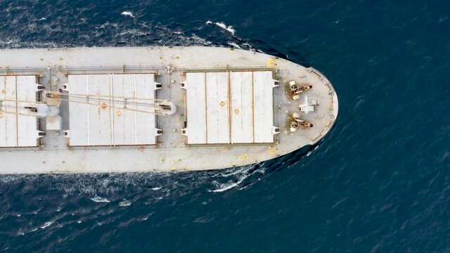 Cargo ship sailing on the ocean to the sea port. A bulk carrier or bulker - a merchant ship specially designed to transport unpackaged bulk cargo - grains, ore, coal or timber. Aerial top down view