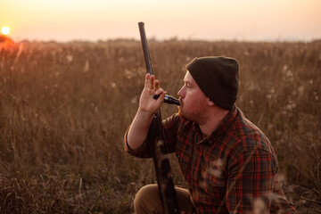 Young red bearded hunter  sitting it grass and blowing at hunter's whistle - photo with selective...