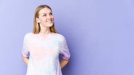 Young blonde woman isolated on purple background relaxed and happy laughing, neck stretched showing...