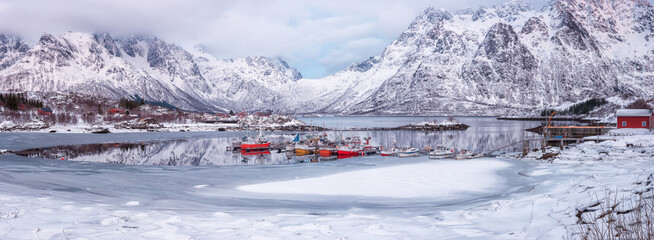 Amazing winter landscape of Northern Norway, scenic panoramic view of the snowy mountains, fjord with fishing boats and cozy small village Laupstad, Lofoten Islands. Outdoor travel background