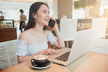 A woman sitting using a laptop and smartphone while eating coffee