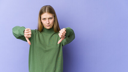 Young blonde woman isolated on purple background showing a dislike gesture, thumbs down....