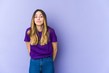 Young caucasian woman isolated on purple background shrugs shoulders and open eyes confused.