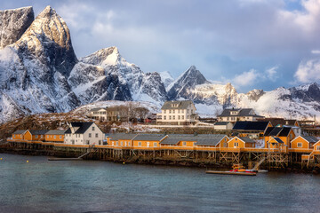 Traditional norwegian fishing houses rorbu on the Lofoten Islands, Hamnoy, Norway. Amazing winter landscape with snowy rocky mountains, water and blue sky with clouds, outdoor travel background