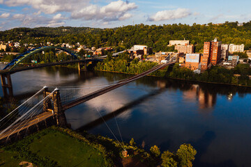 This is an aerial view of the historic Wheeling Suspension Bridge that carries the National Road over the still blue waters of the Ohio River in Wheeling, West Virginia. - 384196767
