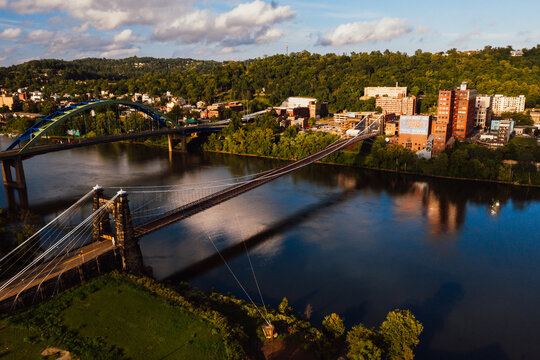 This is an aerial view of the historic Wheeling Suspension Bridge that carries the National Road over the still blue waters of the Ohio River in Wheeling, West Virginia.