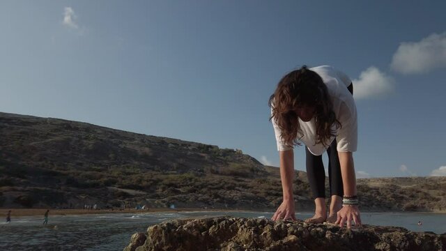 Young caucasian woman is doing yoga and stretching exercises on rock on the beach. High quality 4k footage