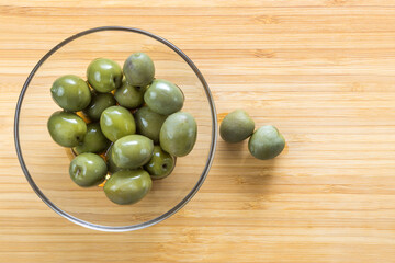 Green olives in a glass plate on a wooden background