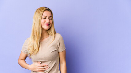 Young blonde caucasian woman touches tummy, smiles gently, eating and satisfaction concept.
