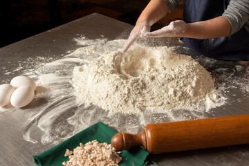 
hands of a girl kneading flour with eggs and rolling pin on steel countertop