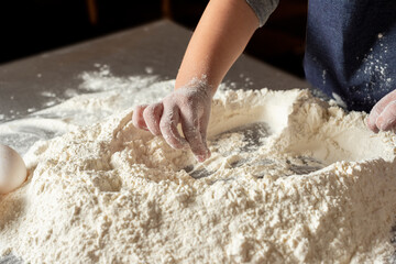 
hands of a girl kneading flour with eggs and rolling pin on steel countertop