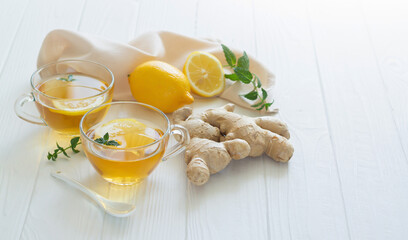 Cups of healthy ginger tea with mint leaves and lemon on white table