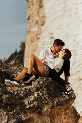 Happy couple are sitting and kissing on the stone mountain. Panorama view from the peak.