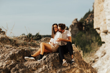 Loving couple sitting on the stones in the mountains. Couple of lovers sitting on a rock and kissing by a wonderful cliff with amazing view.