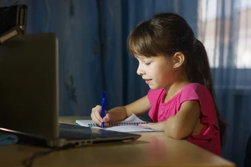 Deurstickers Online onderwijs op afstand. Een schoolmeisje studeert thuis en schrijft huiswerk © Albert Ziganshin