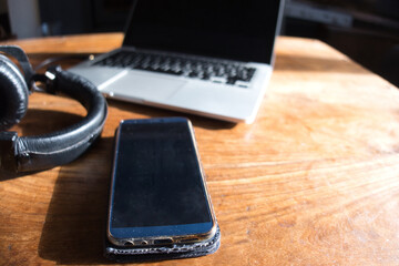 Headphones, smartphone and laptop on coffee table for listening to and editing music and audio.